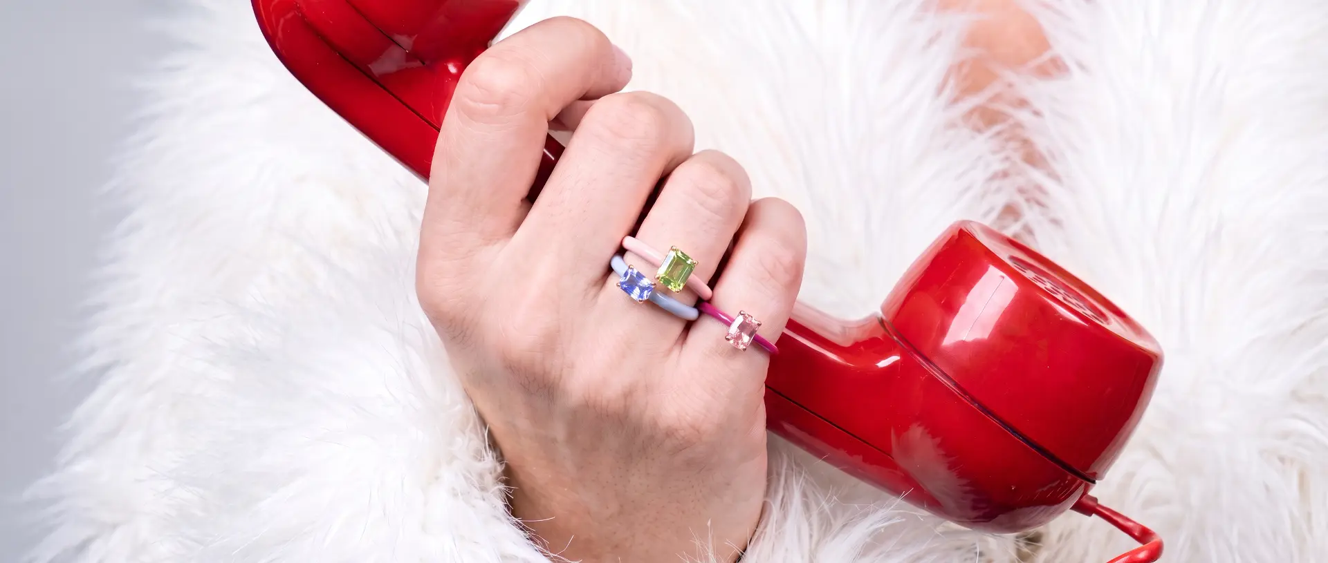 Hand wearing colorful enamel gemstone rings holding a red retro telephone